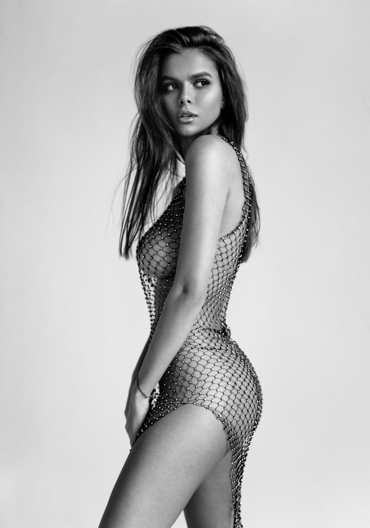 Black and white photo of a magnificent woman in a sheer, studded mesh dress looking over her shoulder