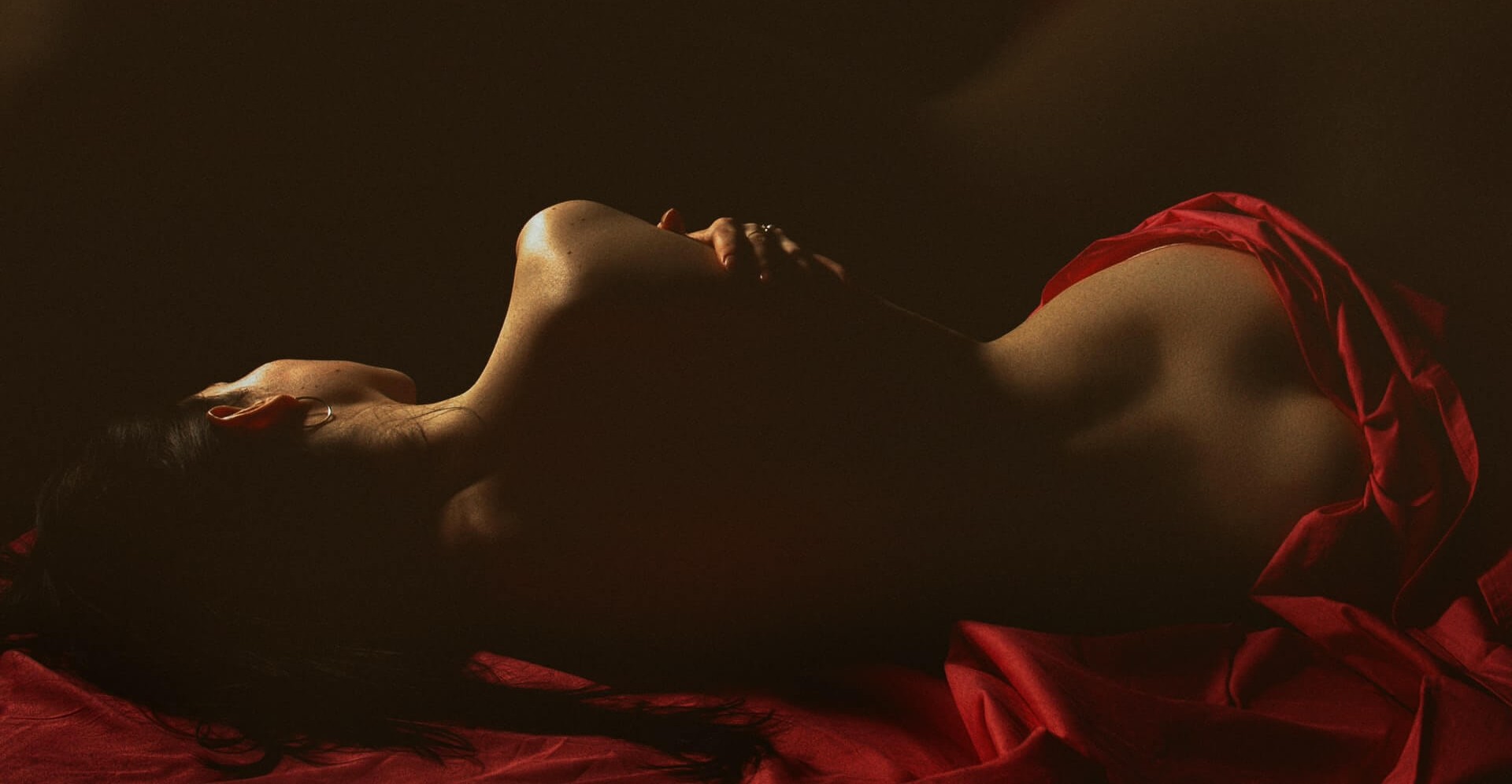 Woman lying on red silk fabric in dark, moody lighting